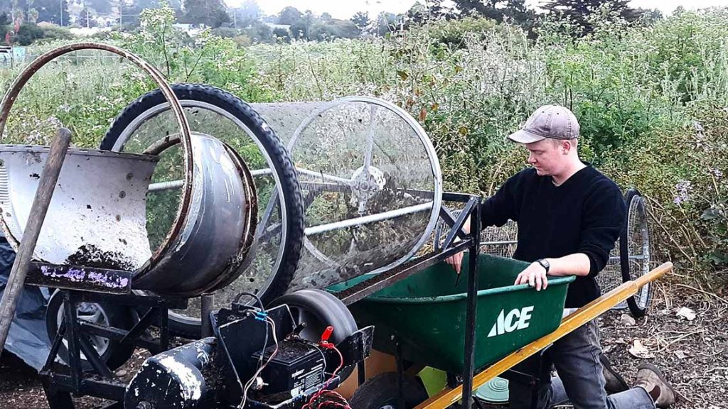 Worker uses sifting device to process finished compost into a wheelbarrow.